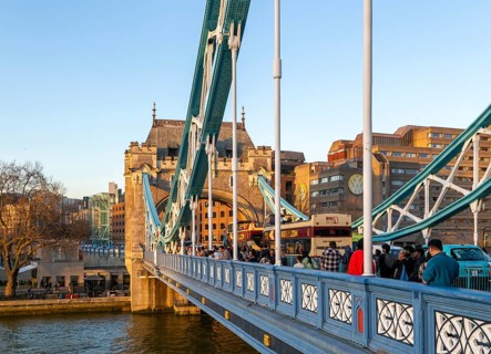 People and open top tour buses cross Tower Bridge in late afternoon, London, England, UK