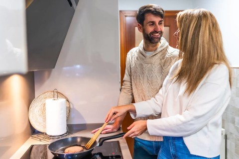 Happy couple preparing dinner together, cooking meat in a pan on the stovetop in their modern