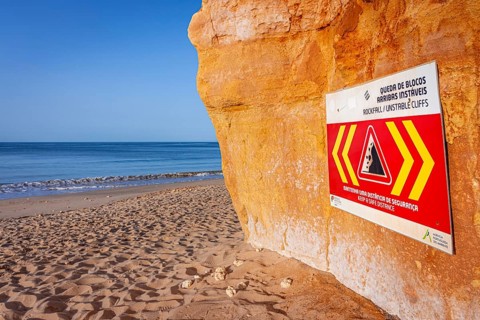 ROCKFALL UNSTABLE CLIFFS, KEEP A SAFE DISTANCE is written in English on a warning sign in Portugal