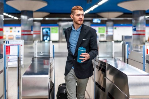 Young professional walking through subway turnstile holding reusable coffee cup, commuting to work
