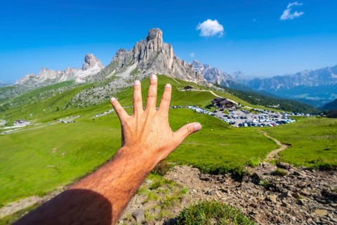 Male tourist showing five fingers with the majestic nuvolau peak and the passo giau mountain pass