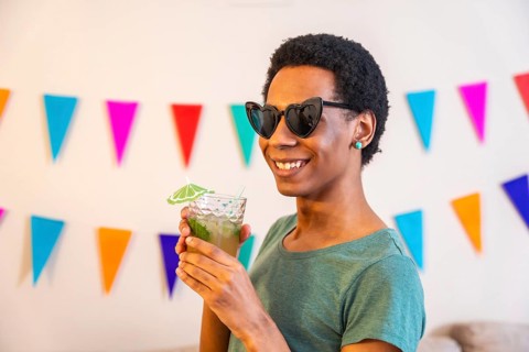 Portrait of a happy latin man with sunglasses drinking cocktail next to garlands decorating a house
