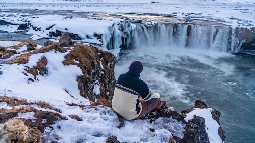 A man sitting looking at the frozen Godafoss waterfall at sunset in winter, Iceland, Europe