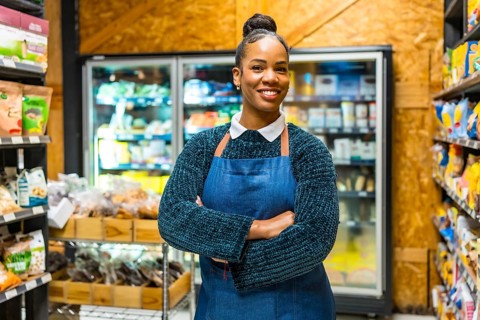 Smiling young african american saleswoman wearing an apron, standing confidently with arms crossed