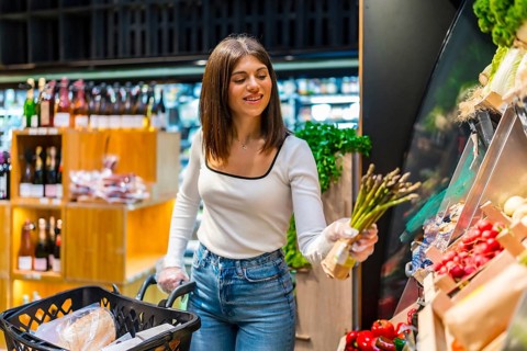 Young woman shopping for fresh asparagus in a supermarket, highlighting healthy eating habits and
