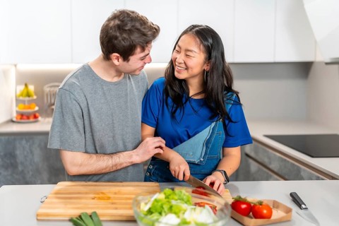 Multiethnic couple sharing a joyful moment while preparing a meal in a sleek, modern kitchen. Fresh