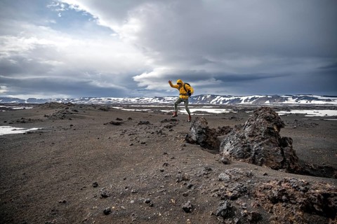 Hiker jumps into the air, snow-covered volcanic landscape with volcanic sand and petrified lava,