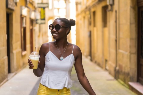 Happy african young woman drinking a iced milkshake while walking along a street