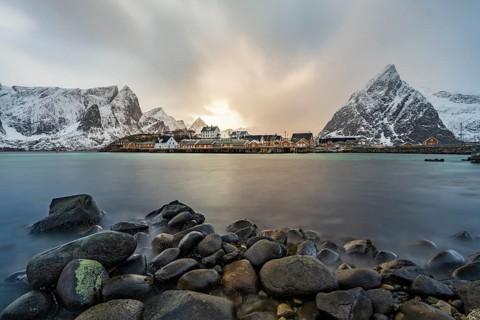 Traditional yellow rorbuer cabins on Sakrisøy Island, snow-capped rocky mountains in the back,