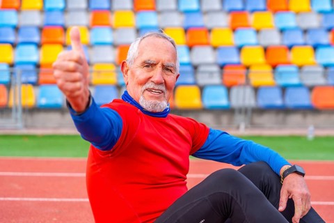 Proud senior man gesturing with thumbs up sitting on a running track after running