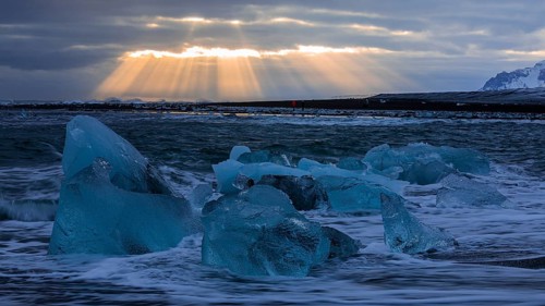 Waves breaking on icebergs on the black beach of Breidamerkursandur, sunset, near Jökullsarlon,