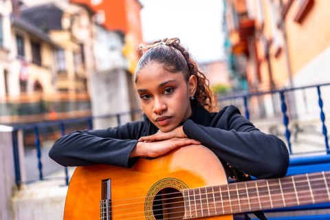 Portrait of a beauty african american woman leaning on an acoustic guitar outside a colorful