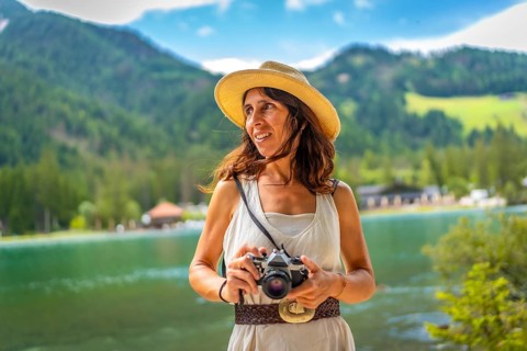 Woman wearing straw hat holding vintage camera enjoying breathtaking view of lake dobbiaco and