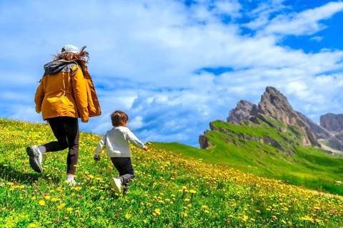 Tourists running on a flowery meadow with the odle and seceda mountains in the background,
