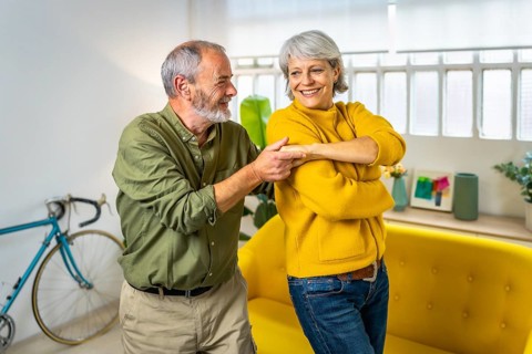 Three quarter length photo of a caucasian senior couple having fun dancing together at home