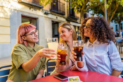 Women toasting and celebrating together sitting on an outdoor bar during sunset in the city
