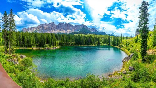 Emerald green water of lake carezza reflecting latemar mountain range in italian dolomites,
