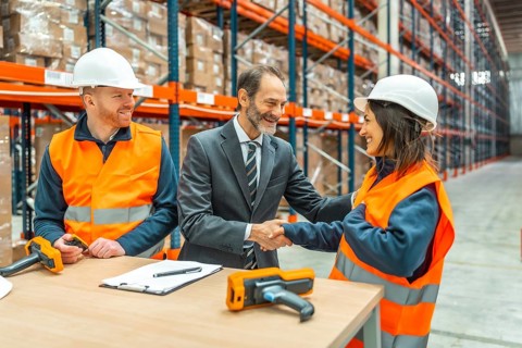 Manager shaking hands with a smiling female worker in a logistics warehouse, a male worker is