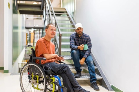 Man with cerebral palsy talking with a work colleague indoors in a modern coworking with staircase