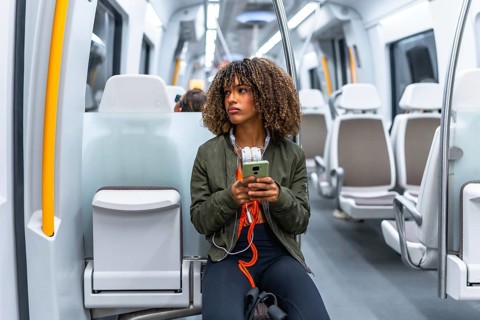 Young beauty latin woman with curly hair sitting distracted on the metro using phone