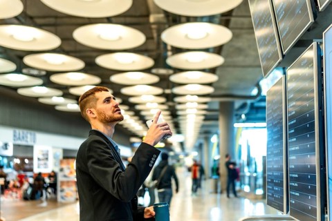 Businessman consulting his smartphone and checking flight information displayed on screens at the