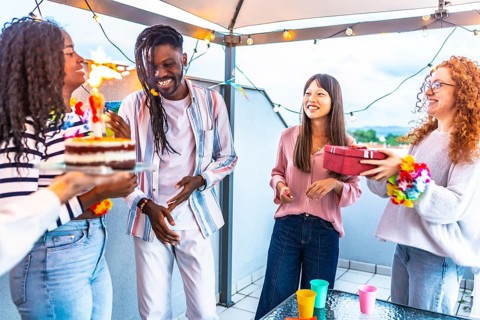 African happy woman receiving a gift and birthday cake celebrating with multi-ethnic friends in a