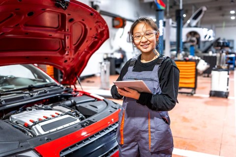 Confident female mechanic using a digital tablet, inspecting a car engine in a professional auto