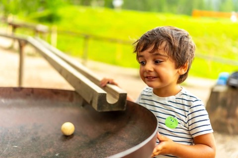 Curious child having fun with a wooden ball rolling down a track in a playground, learning about