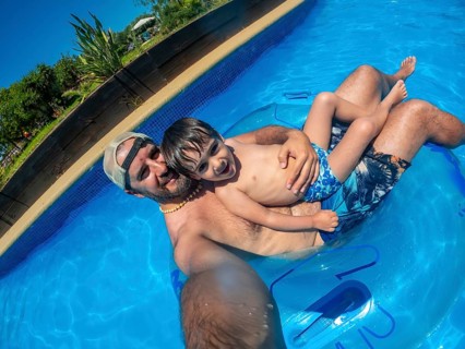 Father and son are taking a selfie while relaxing on an inflatable ring in a swimming pool at a