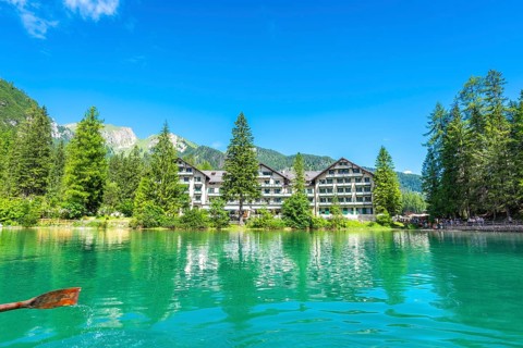 Wooden oar stroking emerald green water of lake braies, with hotel pragser wildsee and dolomites
