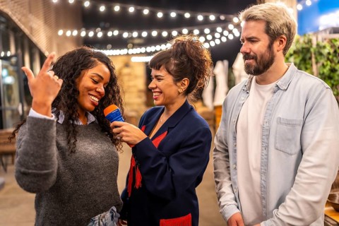 Multi-ethnic happy friends enjoying singing karaoke together at night outdoor party in the terrace