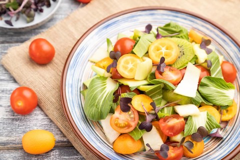 Vegetarian salad of pac choi cabbage, kiwi, tomatoes, kumquat, microgreen sprouts on gray wooden