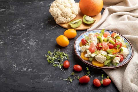 Vegetarian salad of cauliflower cabbage, kiwi, tomatoes, microgreen sprouts on black concrete