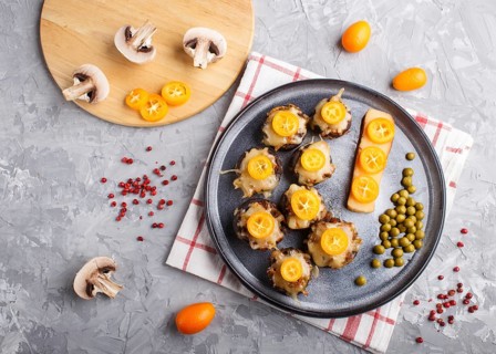 Stuffed fried champignons with cheese, kumquats and green peas on a gray concrete background.