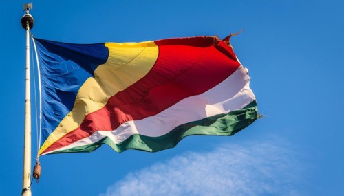 The flag of Seychelles, fluttering in the wind, isolated against a blue sky
