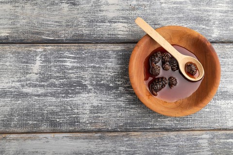 Pine cone jam in wooden bowl on gray wooden background. Top view, flat lay, copy space