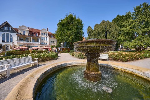 Fountain with benches, trees and houses under a cloudless blue sky in Bad Salzuflen, Lippe