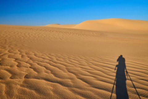 Shadow of a photographer in a vast desert landscape with sand dunes and blue sky, Matruh, Great
