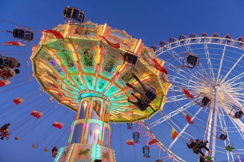 Illuminated carousel and Ferris wheel at night in a lively amusement park, funfair, wave flight,