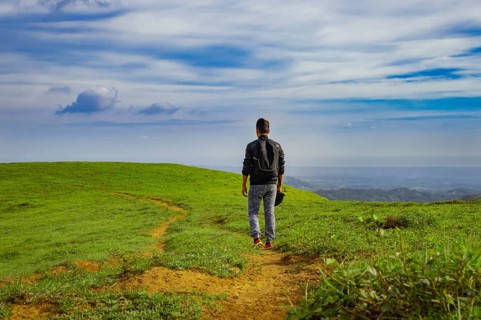 Backpacker walking on a beautiful hill. View of backpacker man walking on the beautiful hill