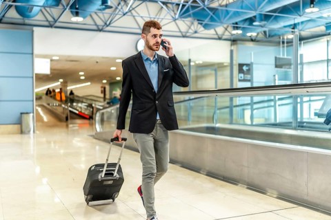 Businessman pulling a suitcase while talking on the phone, confidently walking through a bustling