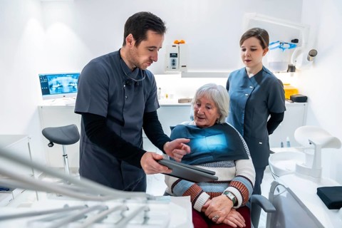 Dentist and nurse explaining radiography to a senior patient sitting in a dental chair, during a