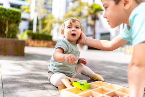 Close-up of a bother caressing a baby boy playing with toys in a park