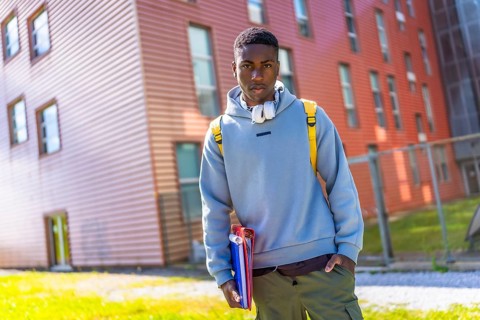 Cool african student with hoodie and rucksack holding folders outside the university