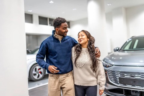 Happy multiethnic couple buying a new electric car at a dealership, hugging each other and smiling