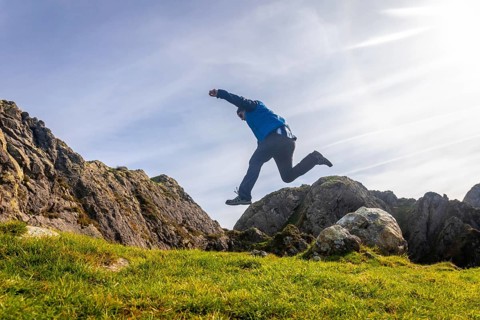 Male hiker jumping on a green meadow in front of the rocky peaks of aiako harria or penas de aia