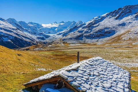 Alpine hut with snow-covered roof, slightly snow-covered alpine meadow, behind the Moiry glacier,