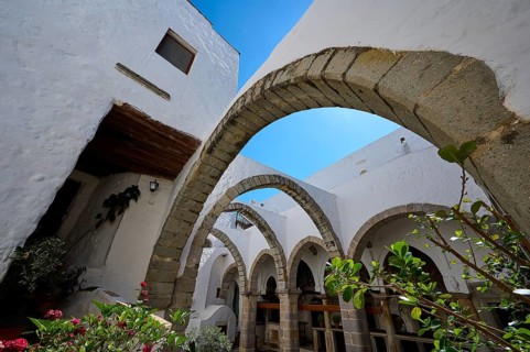 Inner courtyard with stone arches, plants and white walls under a blue sky in a Mediterranean