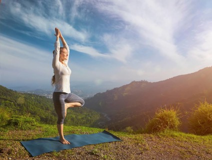 Yoga practice outdoors, woman practices balance yoga asana Vrikshasana tree pose in Himalayas