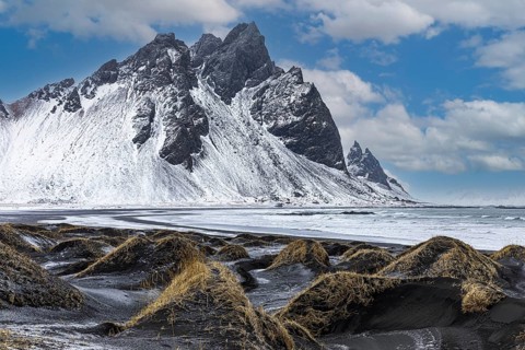 Black sand dunes with reed remains, behind them snowy rocky slopes of Vestrahorn, near Höfn,